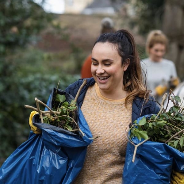 A volunteer tidying a garden, carrying two bags of green waste.
