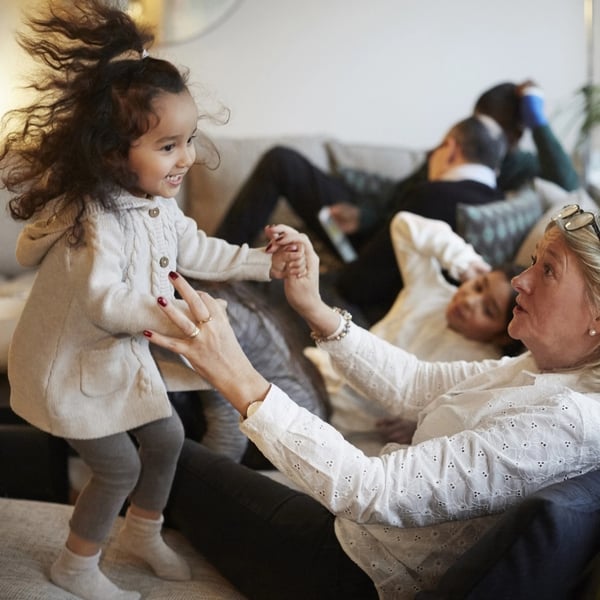 A family lounging on a sofa with grandmother and granddaughter playing in the foreground.