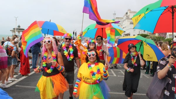 A crowd of people raising rainbow flags and umbrellas during a Pride parade in Brighton & Hove, UK.