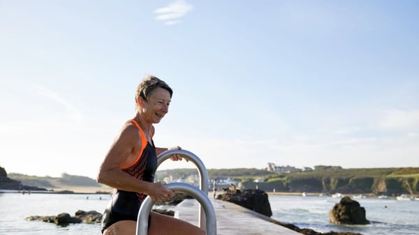 A senior woman getting into a tidal swimming pool on a bright sunny day.