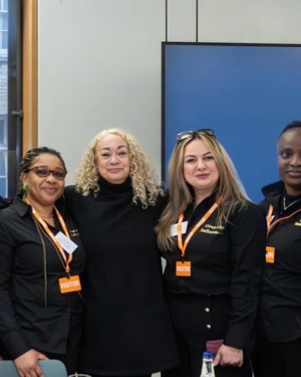 Six people stand together indoors, all wearing black clothing and orange visitor badges.