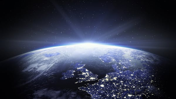 Earth seen from space with sunlight rising over Europe and city lights visible at night.