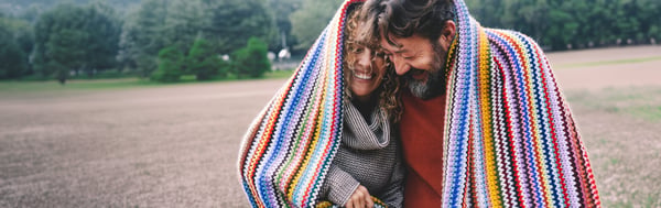 Two people wrapped in a colourful striped blanket walking together in an open park.