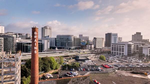 Cityscape of central Cardiff featuring the Brains Brewery chimney, Cardiff Interchange, train lines and roads in the foreground under a partly cloudy sky.