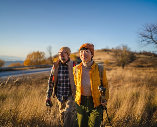 Two people walking through the countryside with hiking gear on a sunny autumn day.