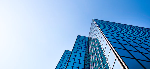 Modern glass office buildings viewed from below against a clear blue sky.