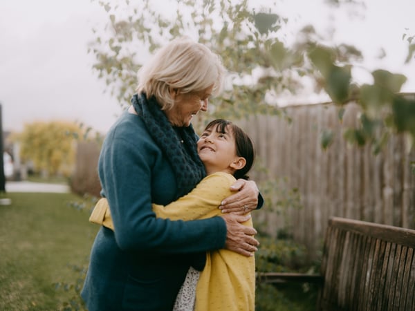 Older adult hugging a child outdoors in a garden.
