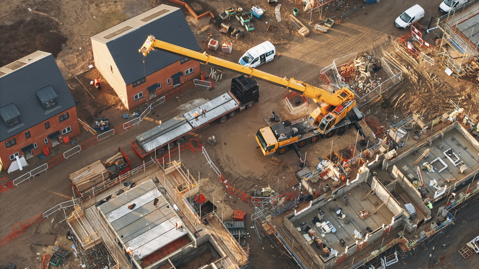 Aerial view of a construction site with houses in various stages of building and a large yellow crane lifting materials. Aerial view of a construction site with houses in various stages of building and a large yellow crane lifting materials.