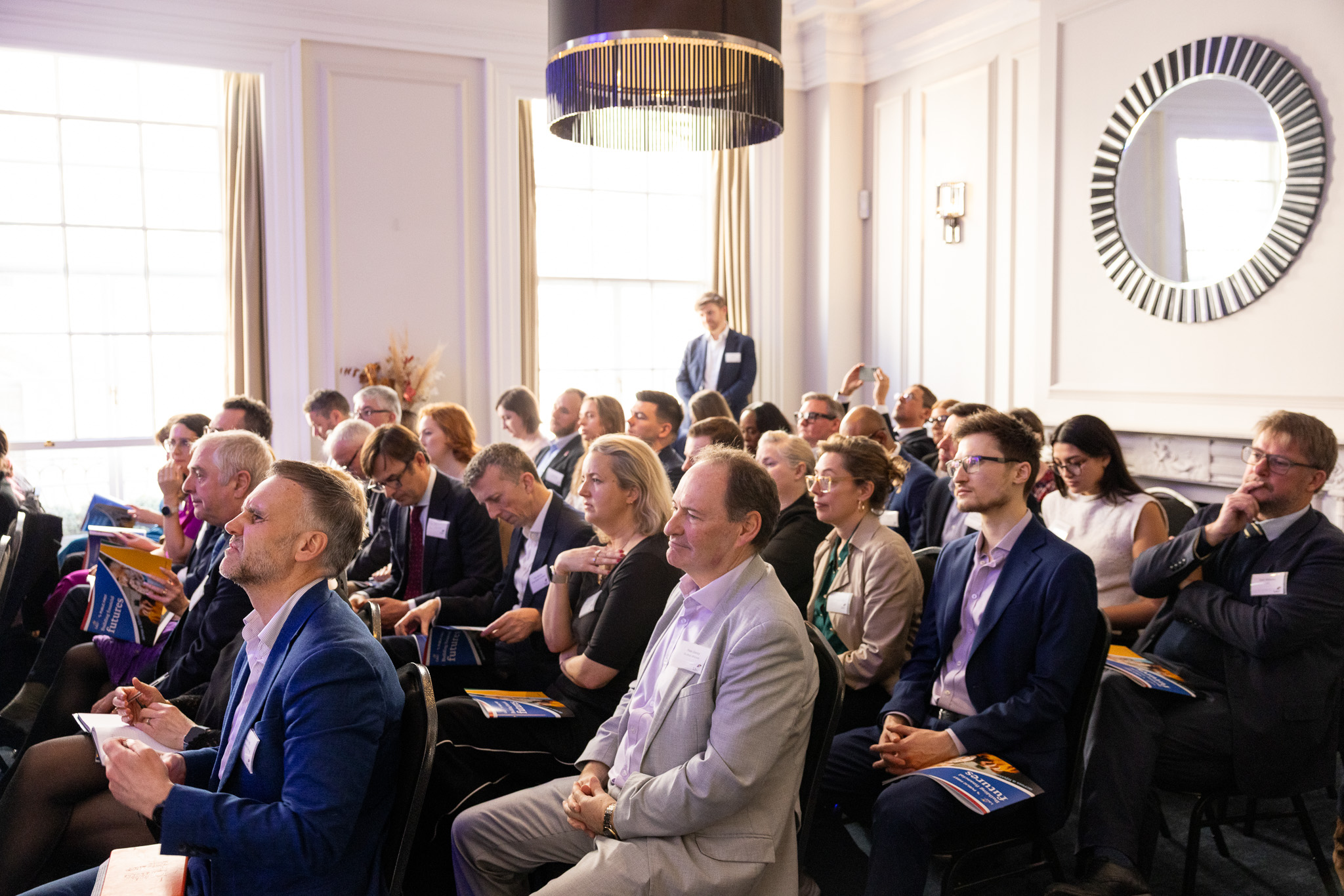 Attendees seated closely together reading brochures and event materials during a session.