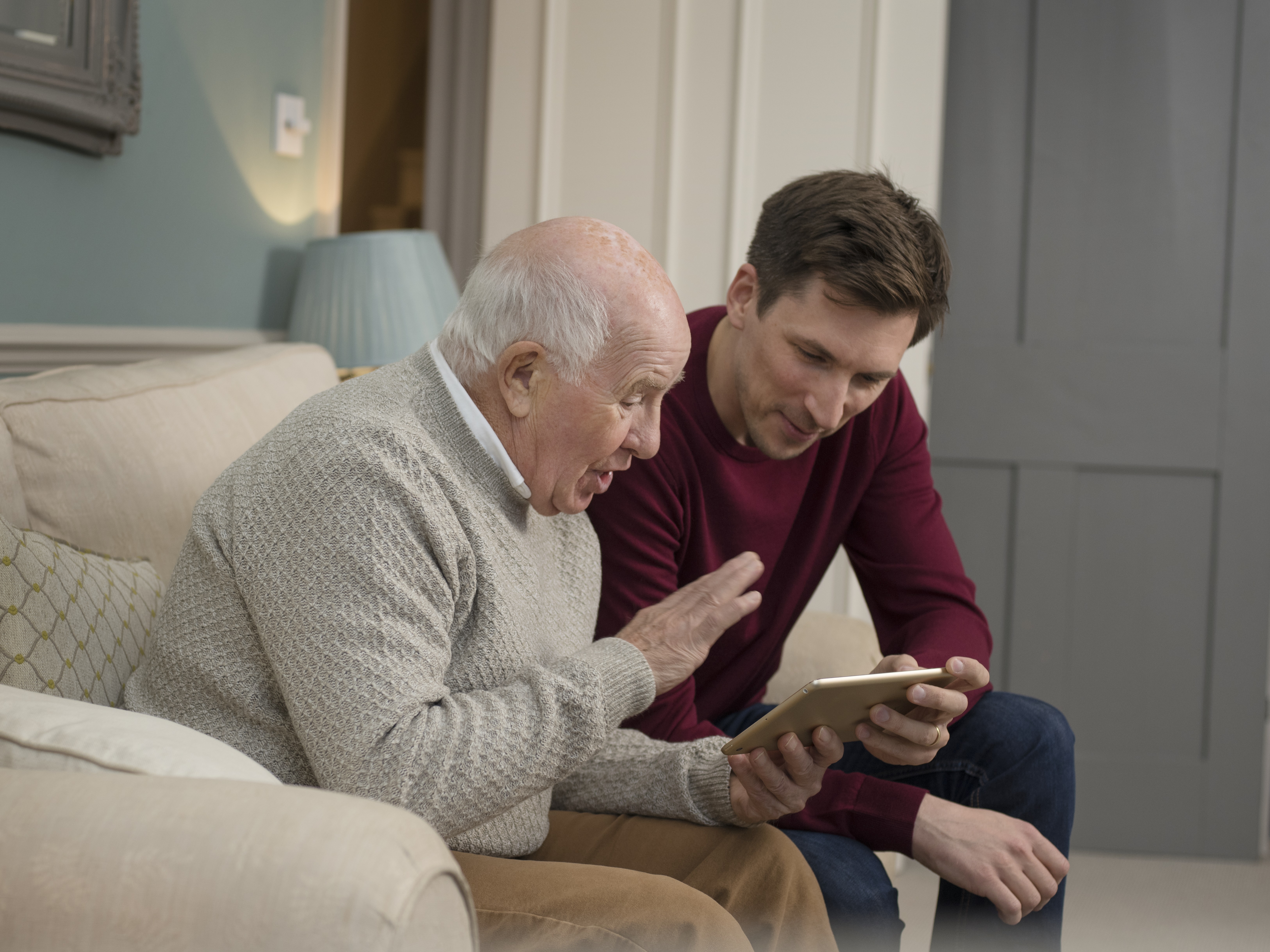 Middle aged male helping elderly male with touch screen 