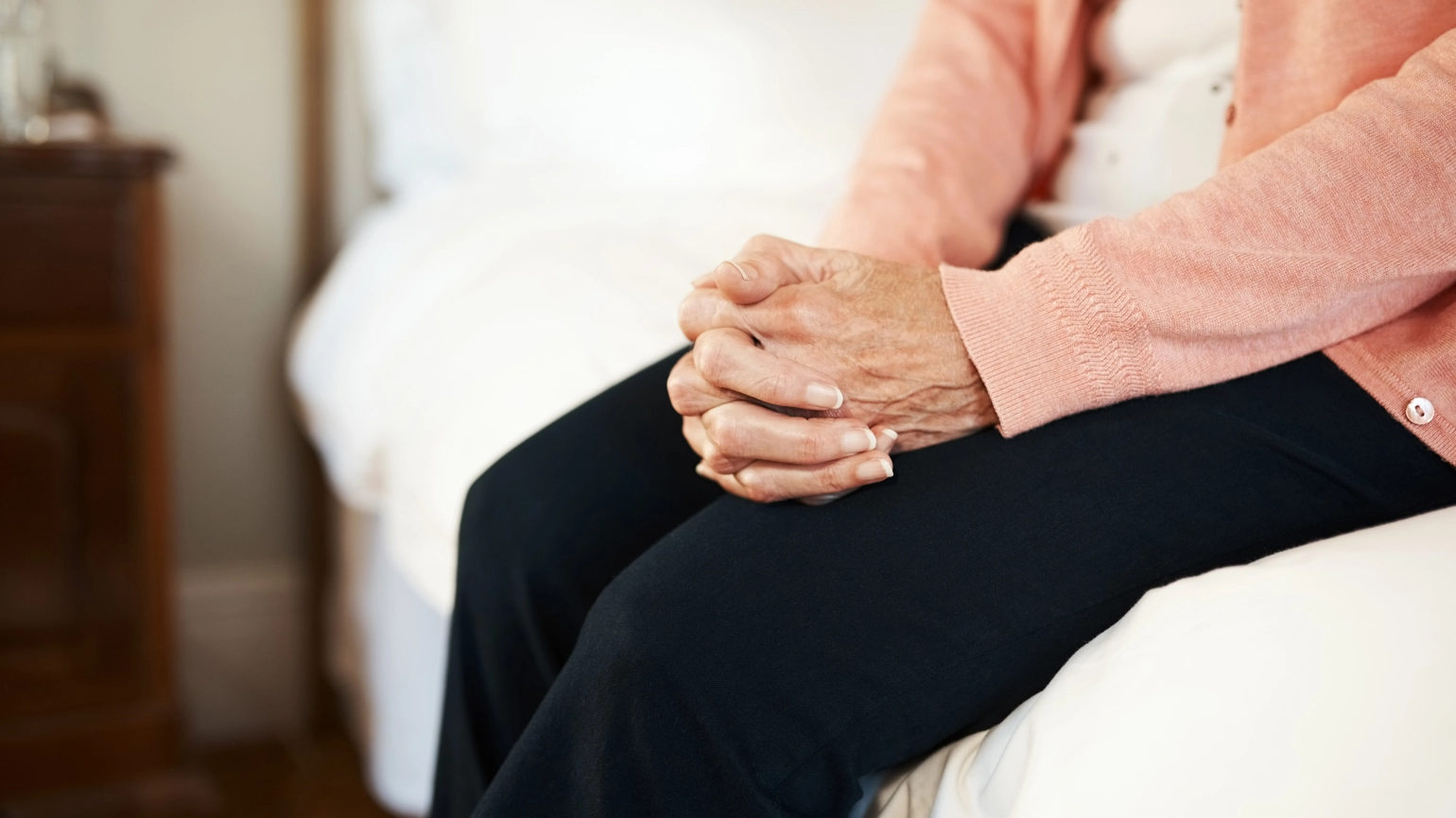 Female sitting at edge of bed holding her hands  Female sitting at edge of bed holding her hands