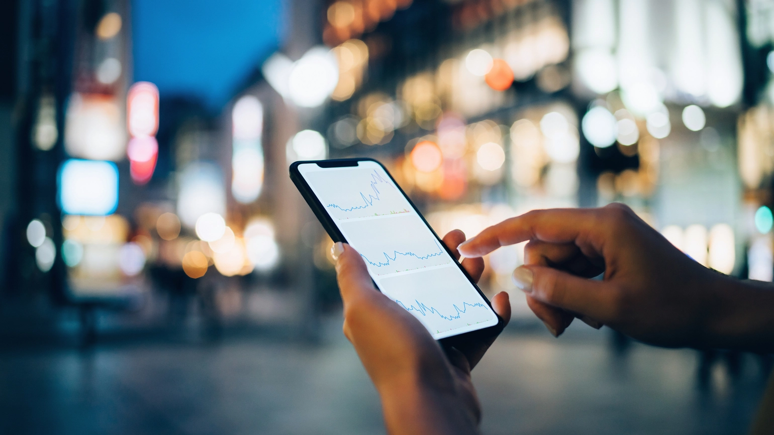 Photo of hand checking charts through phone in the street Photo of hand checking charts through phone in the street