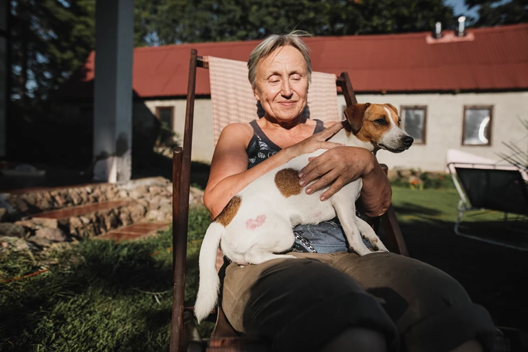 Older woman with a dog on her lap, sitting in a garden chair