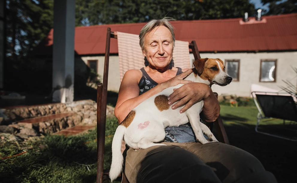 Older woman with a dog on her lap, sitting in a garden chair