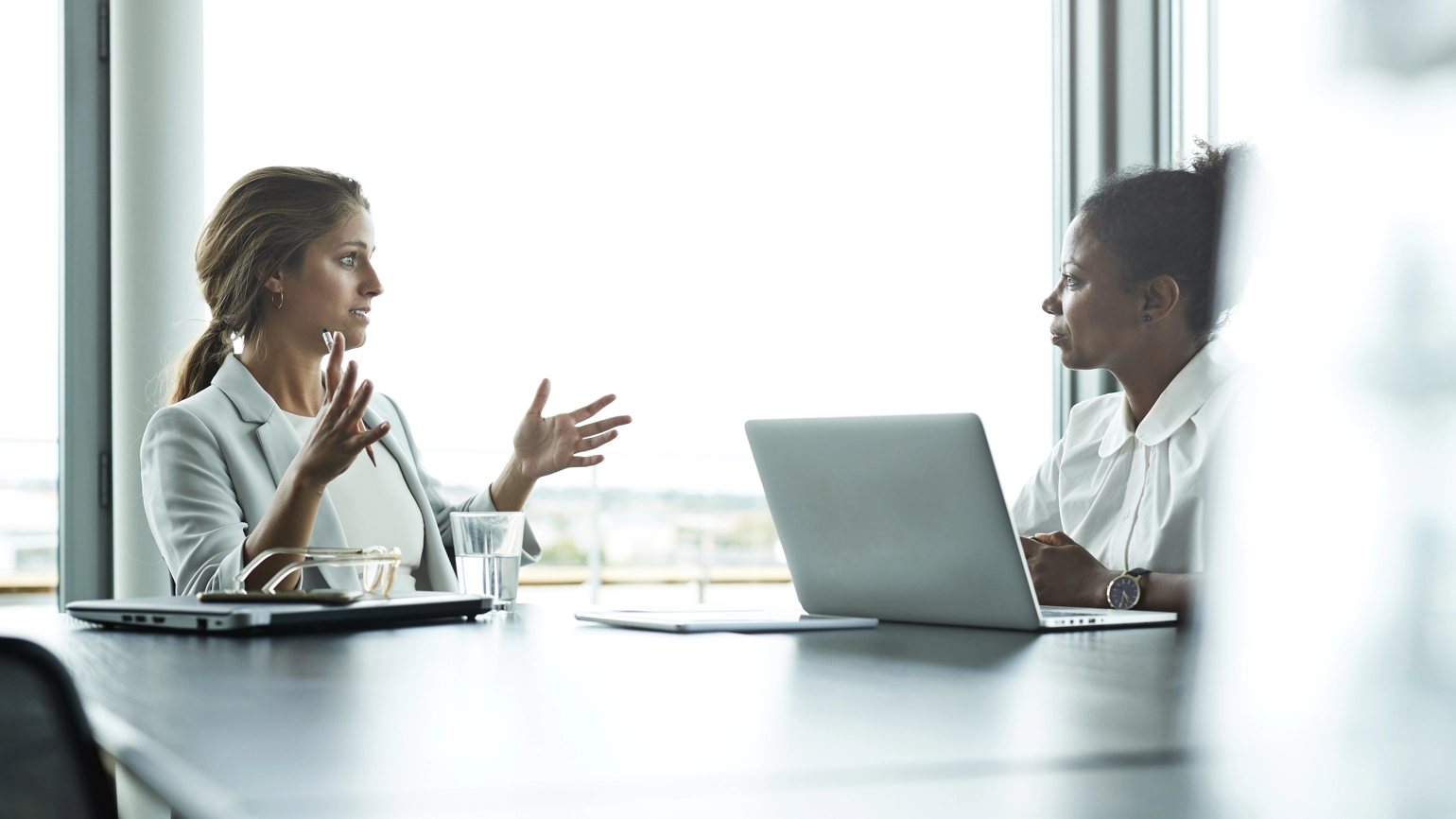 Two female in a business environment chatting in the meeting room with paper works and laptop around Two female in a business environment chatting in the meeting room with paper works and laptop around