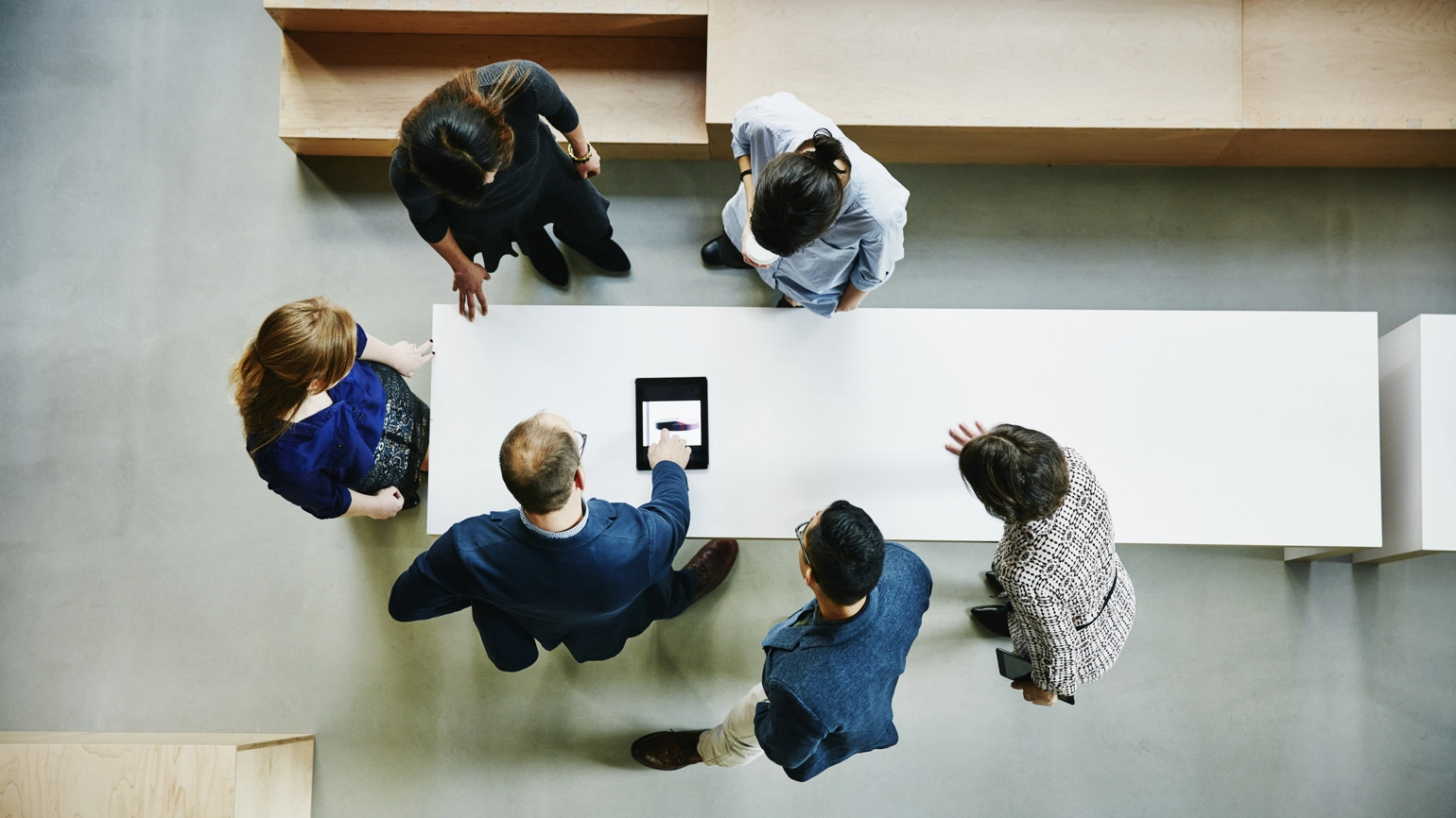 Photograph with birds eye view of office workers around a table working together Photograph with birds eye view of office workers around a table working together