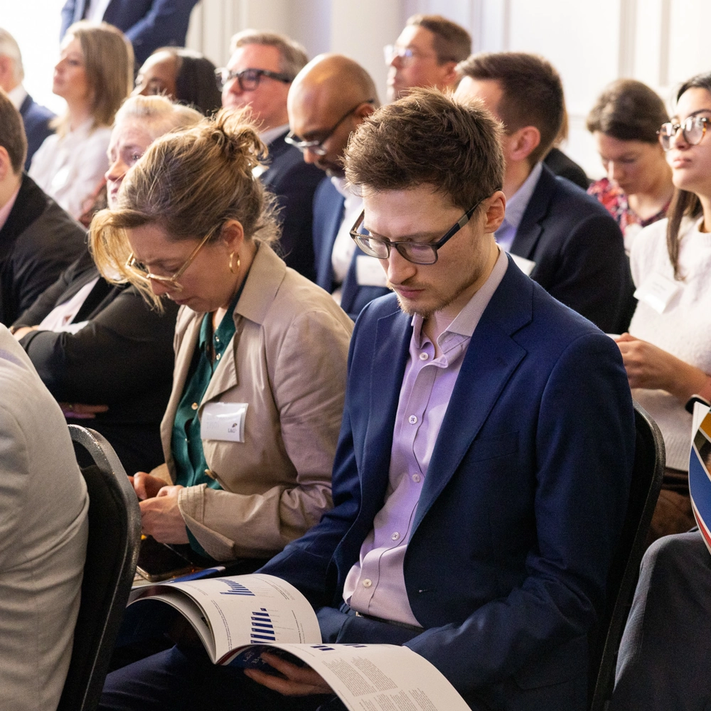 Audience seated in rows in a bright event room holding brochures and listening to a presentation. Audience seated in rows in a bright event room holding brochures and listening to a presentation.