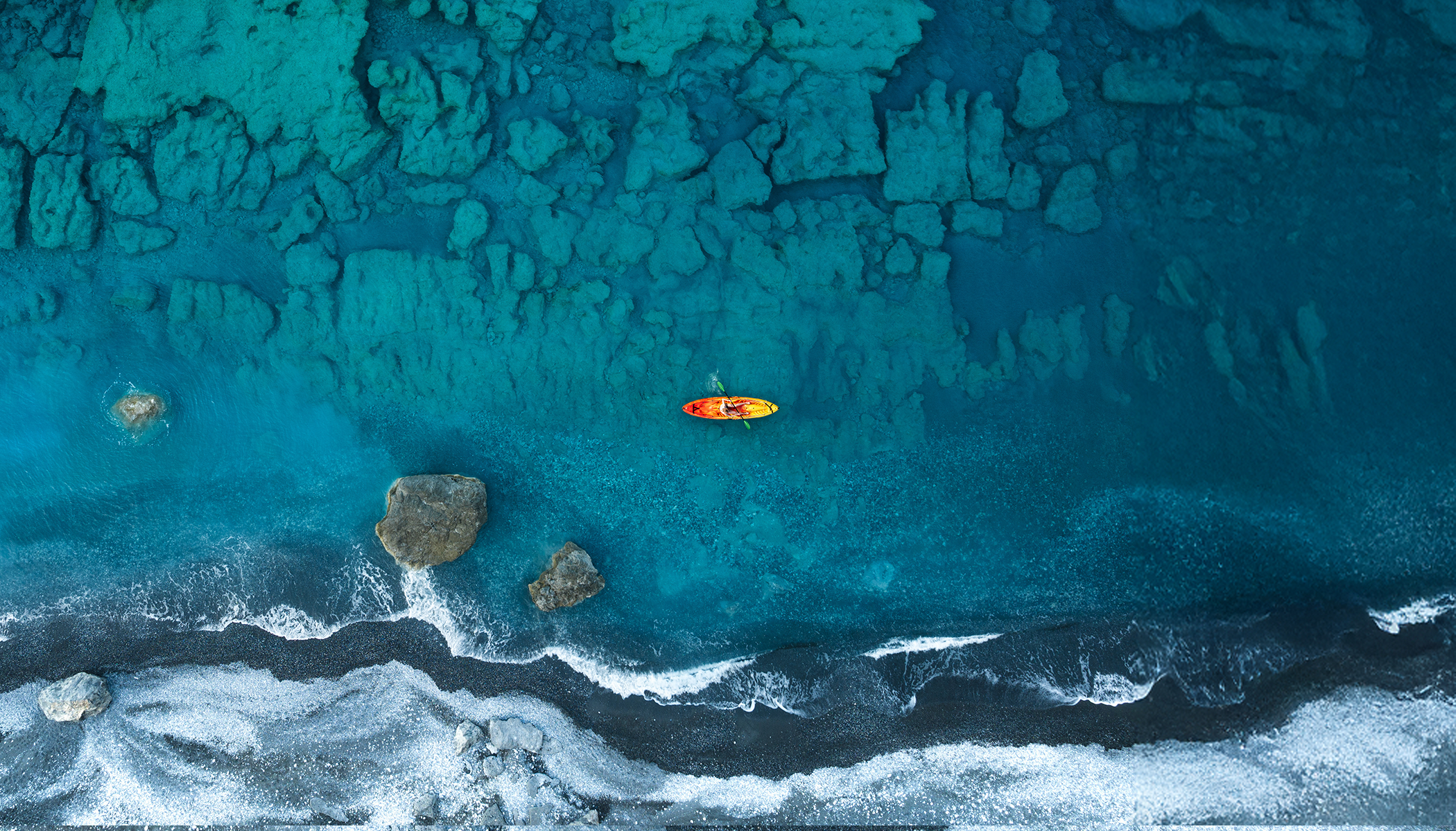 Aerial drone view of a lone kayak gliding over the turquoise waters of Agios Pavlos beach, Crete, Greece, surrounded by coastline.