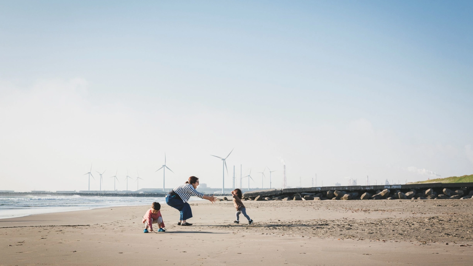 Mother and two kids playing in the beach showing wind farm behind  Mother and two kids playing in the beach showing wind farm behind