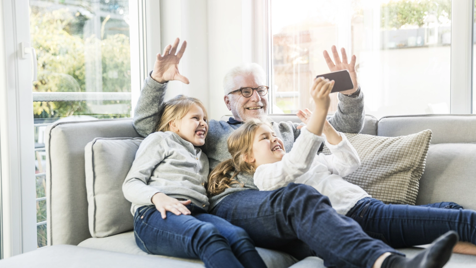 Grandfather and two granddaughters taking photo with their phone in living room sofa Grandfather and two granddaughters taking photo with their phone in living room sofa