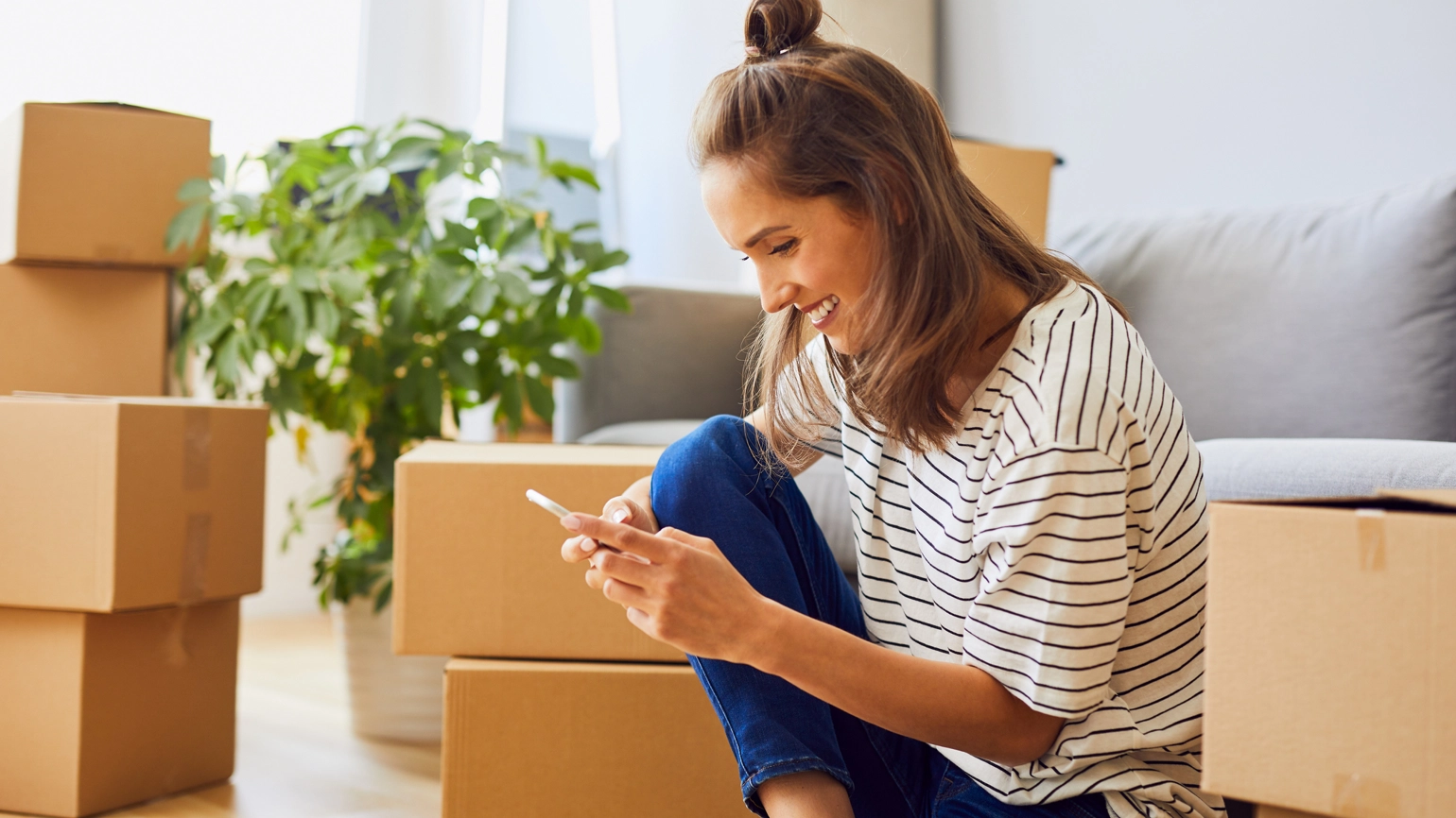 Young female checking her phone and smile with her unpacked moving box around Young female checking her phone and smile with her unpacked moving box around