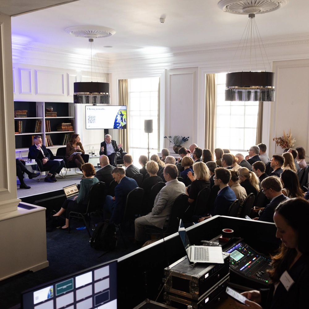 Wide view of a conference room showing the audience, panel speakers, and technical equipment at the back. Wide view of a conference room showing the audience, panel speakers, and technical equipment at the back.