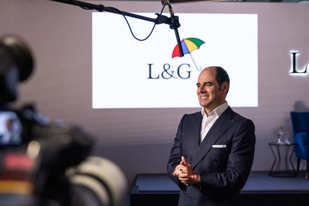 António Simões is standing in front of an empty stage, with the L&G logo projected on the wall. He is wearing a dark suit and white shirt, with his hands clasped in front of him. A microphone boom is positioned above him, and there are cameras and lighting equipment visible in the foreground.  António Simões is standing in front of an empty stage, with the L&G logo projected on the wall. He is wearing a dark suit and white shirt, with his hands clasped in front of him. A microphone boom is positioned above him, and there are cameras and lighting equipment visible in the foreground.