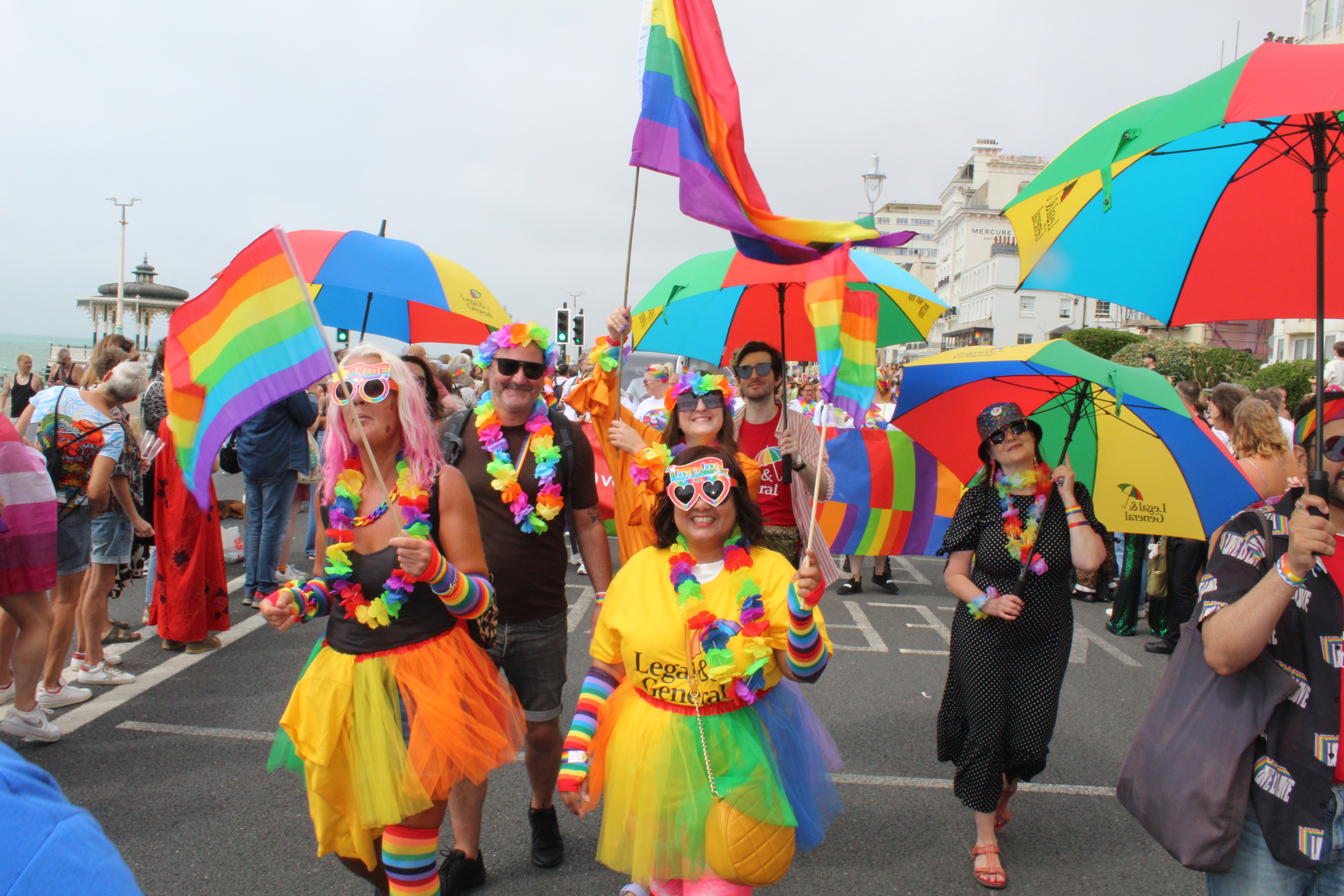 A pride parade with L&G employees waving rainbow flags and carrying L&G branded umbrellas.