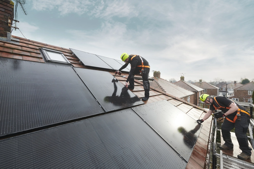 Two workers installing solar panels on a sloped roof, wearing safety harnesses and helmets Two workers installing solar panels on a sloped roof, wearing safety harnesses and helmets