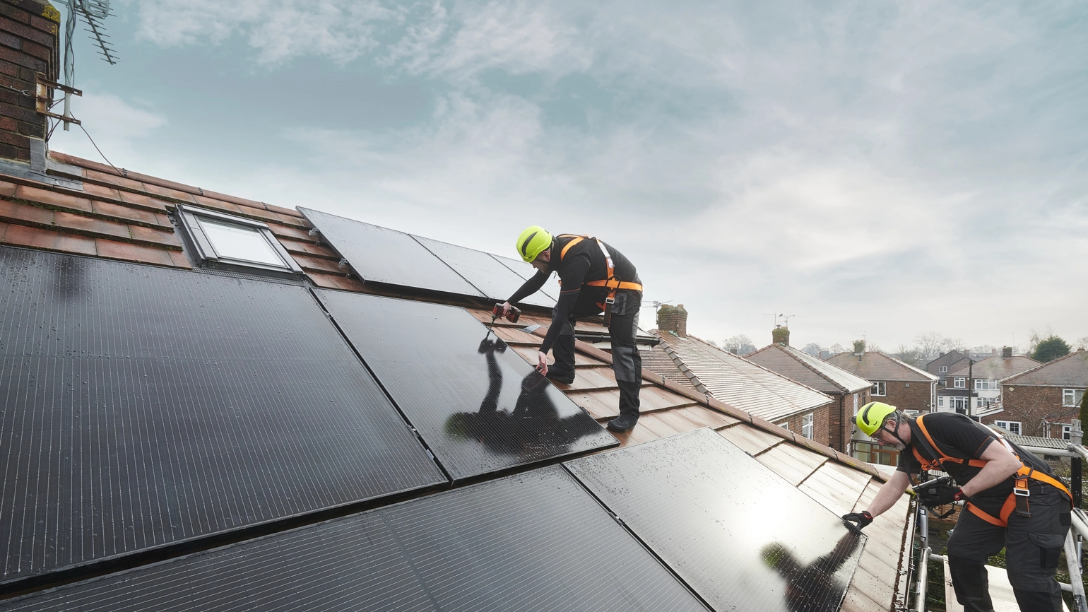 Two workers installing solar panels on a sloped roof, wearing safety harnesses and helmets Two workers installing solar panels on a sloped roof, wearing safety harnesses and helmets