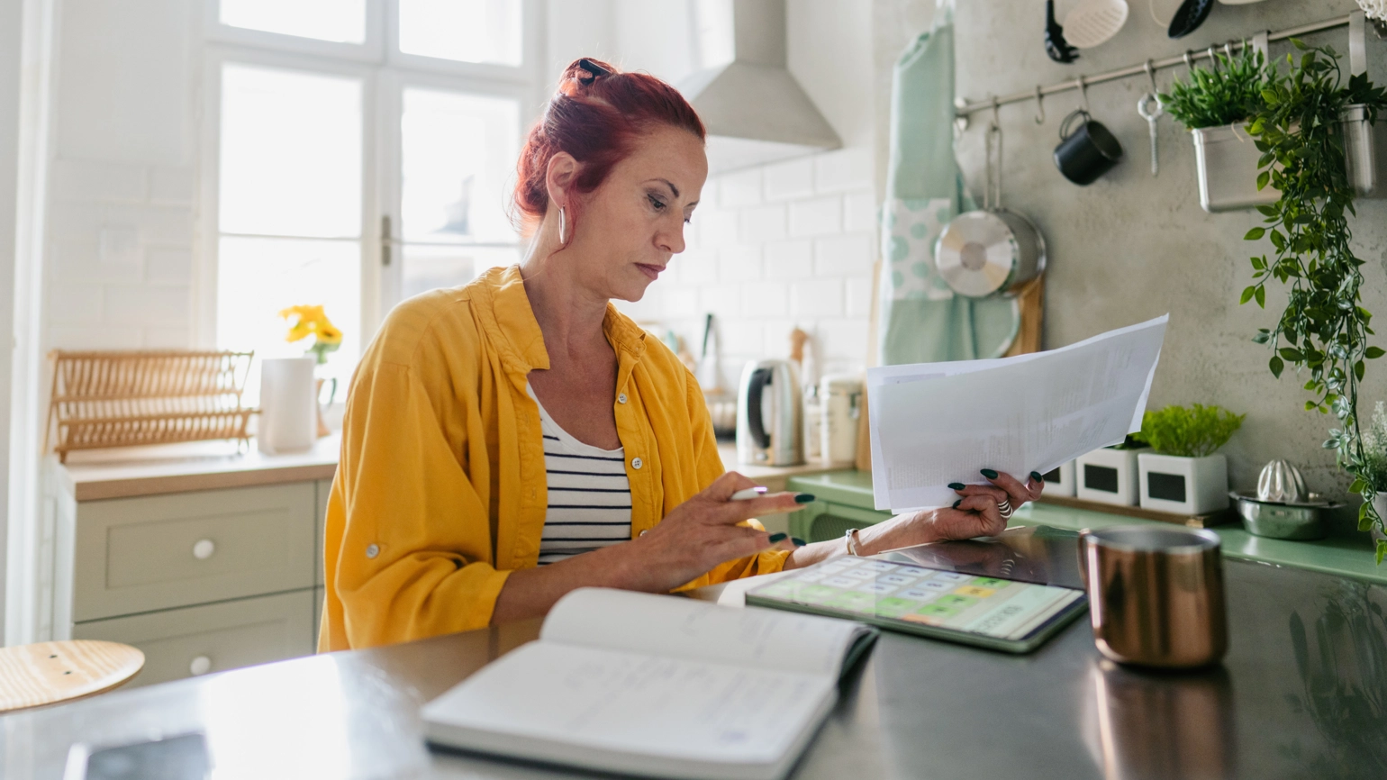 Middle aged female checking bills in her kitchen Middle aged female checking bills in her kitchen