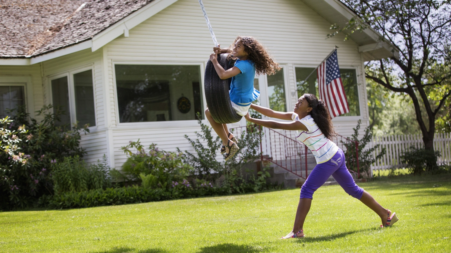 Two young girls playing in their front garden pushing swings Two young girls playing in their front garden pushing swings
