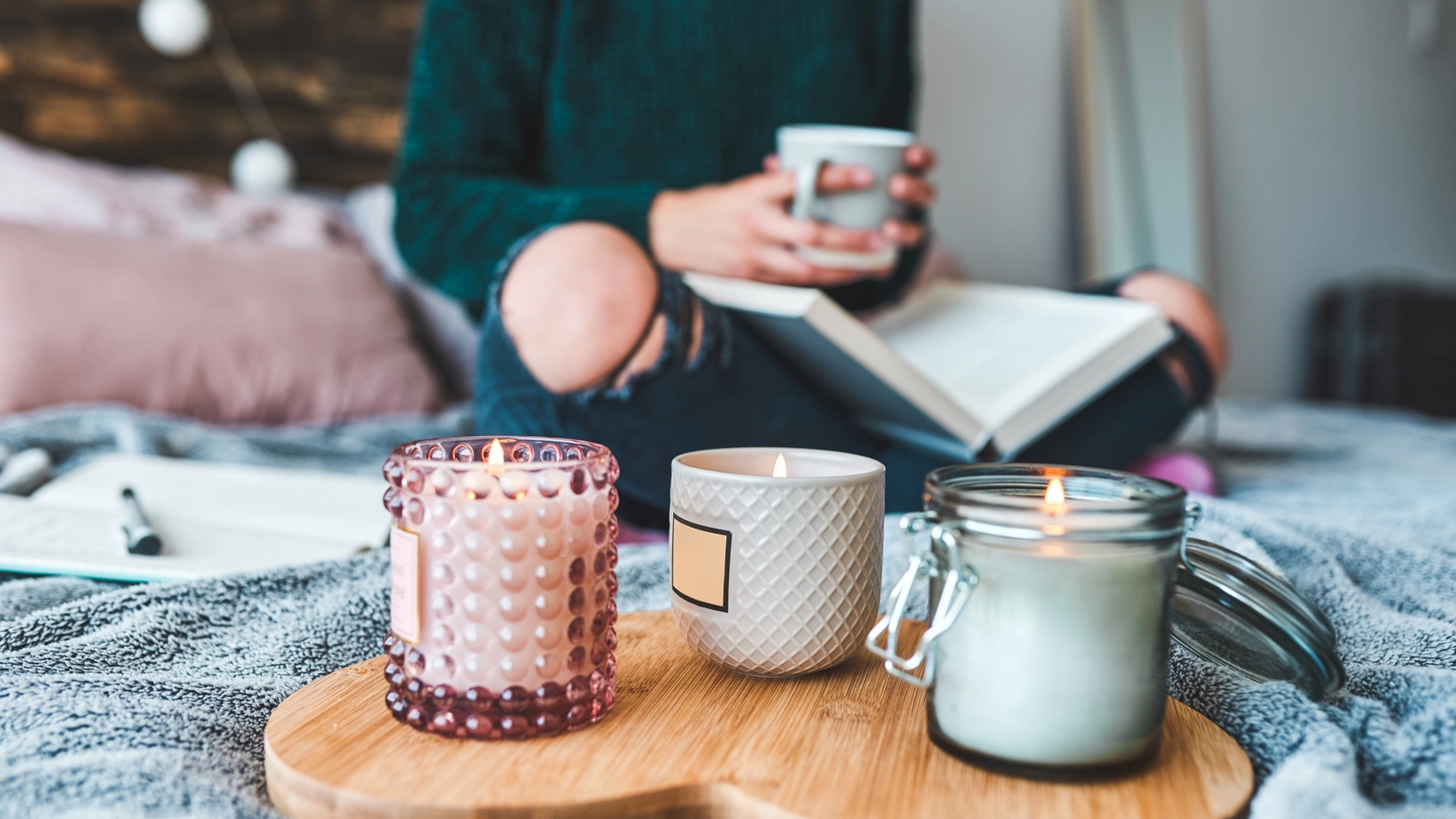Three scented candles in bed with a female holding mug Three scented candles in bed with a female holding mug
