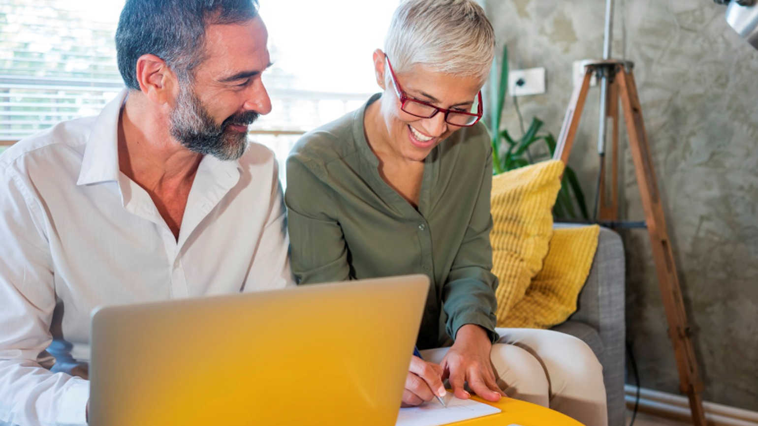 Middle aged couple checking paper documents with their laptop in the livingroom Middle aged couple checking paper documents with their laptop in the livingroom