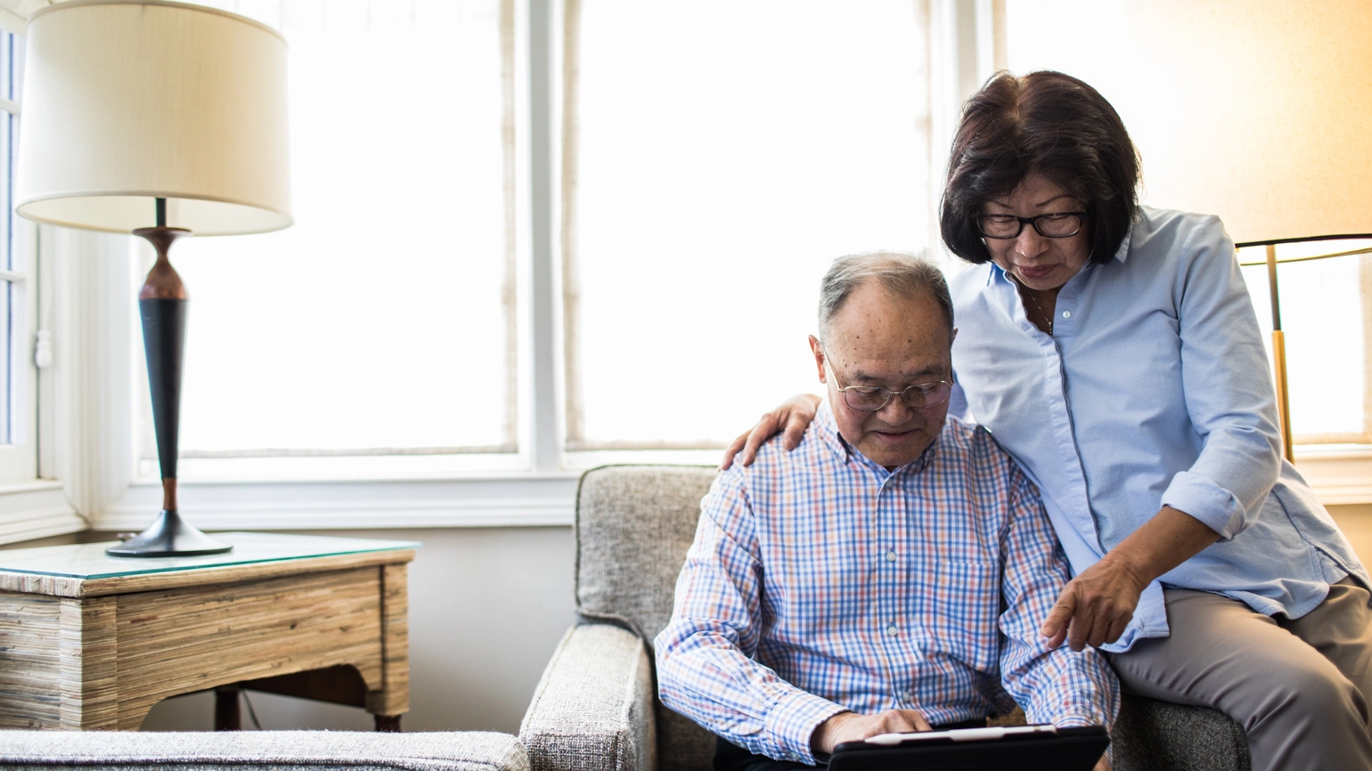 Elderly couple checking touch screen in their living room arm chair  Elderly couple checking touch screen in their living room arm chair