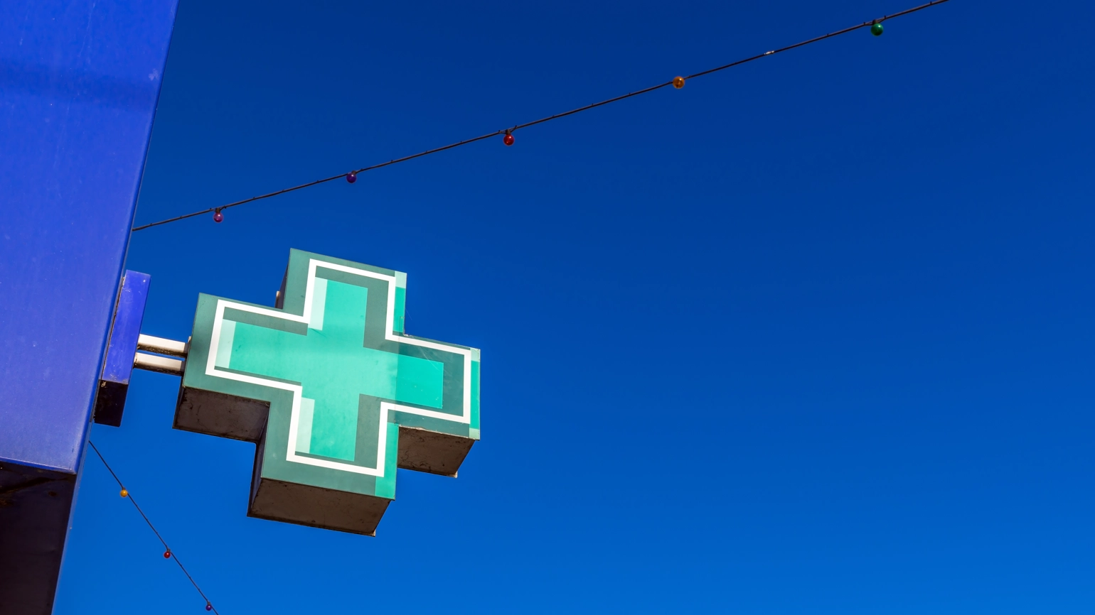 A high-angle view of a green pharmacy cross sign mounted on the exterior of a building, set against a clear blue skies. A high-angle view of a green pharmacy cross sign mounted on the exterior of a building, set against a clear blue skies.