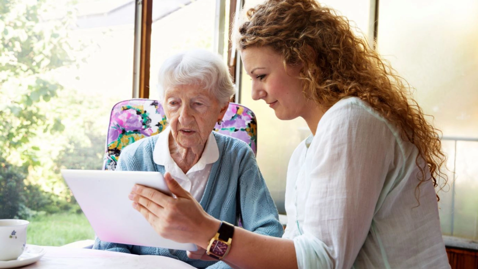 Female helping elderly female to use touch screen Female helping elderly female to use touch screen