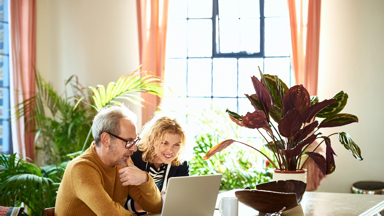 Middle aged couple checking laptop together in their living room dining table  Middle aged couple checking laptop together in their living room dining table