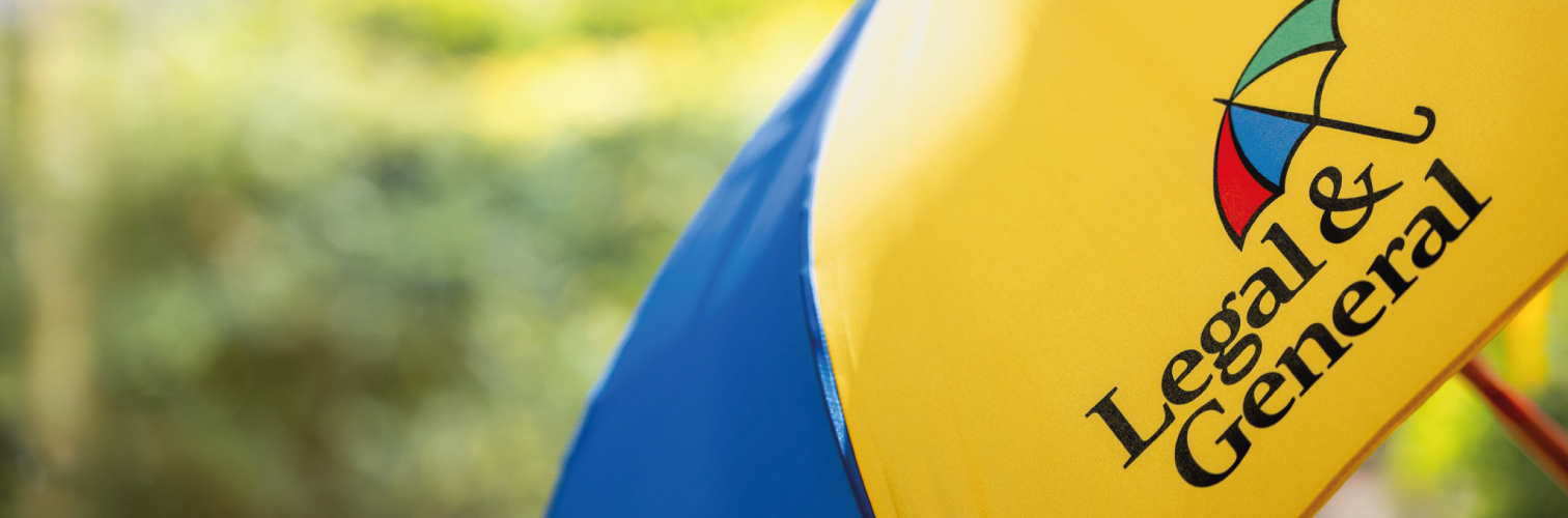 A close up of a colourful Legal & General umbrella, in a sunny and green outdoor setting.