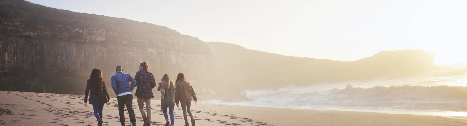 Group of friends walking across a sandy beach at sunset Group of friends walking across a sandy beach at sunset