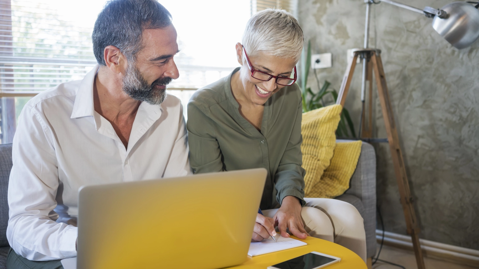 Middle aged couple checking paper works together in the living room with their laptop on Middle aged couple checking paper works together in the living room with their laptop on