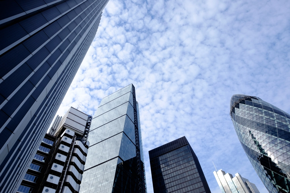 Upward view of modern skyscrapers and office blocks in a central London, UK, featuring glass facades and distinctive architectural designs, set against a blue sky with light clouds. Upward view of modern skyscrapers and office blocks in a central London, UK, featuring glass facades and distinctive architectural designs, set against a blue sky with light clouds.