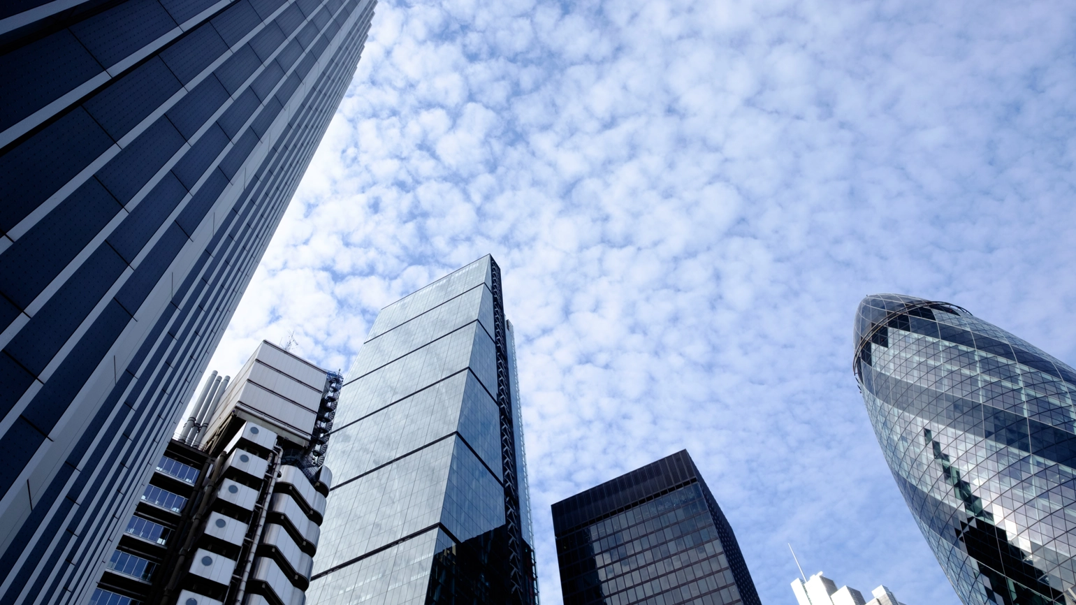 Upward view of modern skyscrapers and office blocks in a central London, UK, featuring glass facades and distinctive architectural designs, set against a blue sky with light clouds. Upward view of modern skyscrapers and office blocks in a central London, UK, featuring glass facades and distinctive architectural designs, set against a blue sky with light clouds.