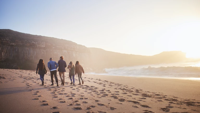 Group of friends walking across a sandy beach at sunset
