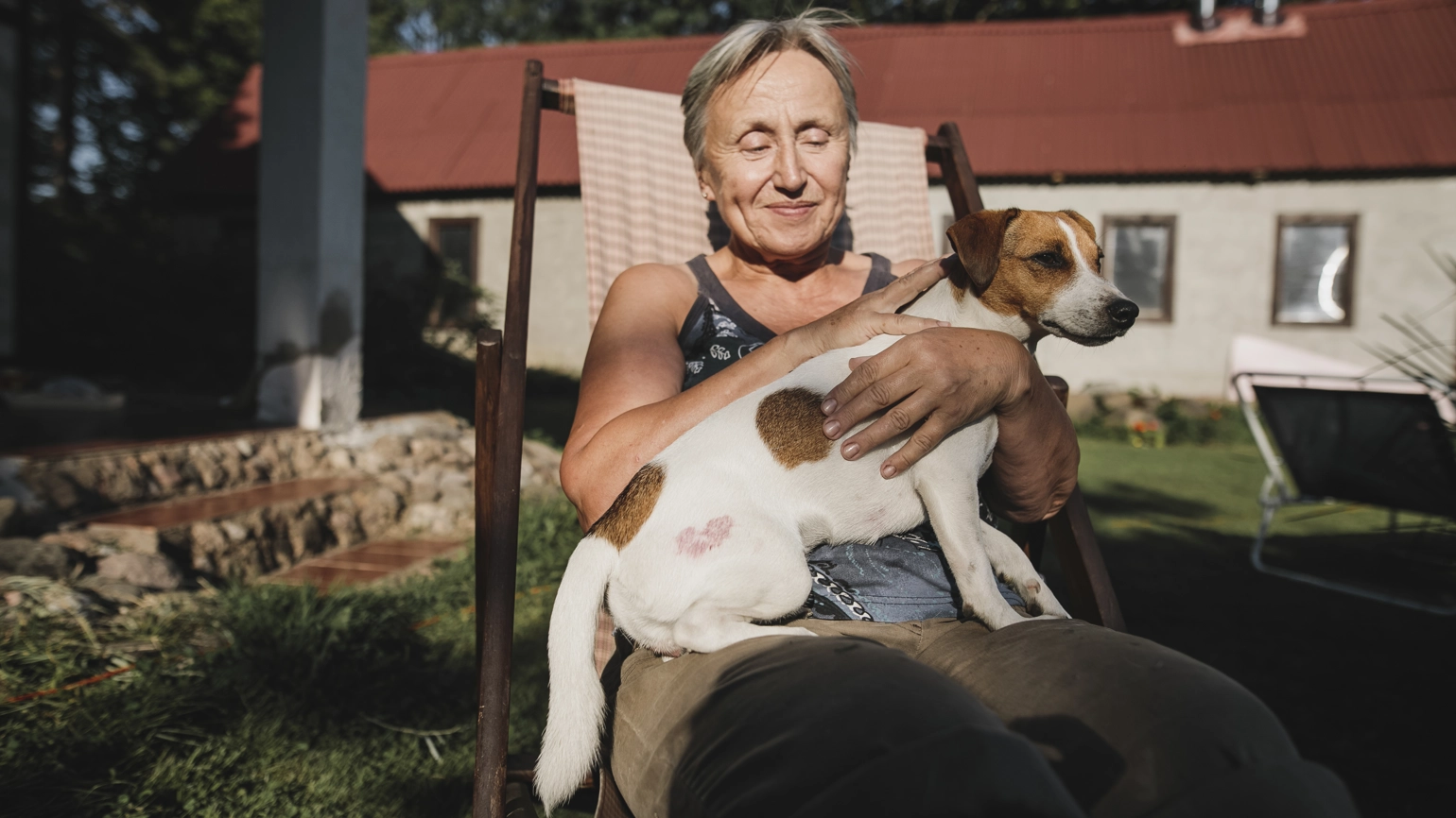 Older woman with a dog on her lap, sitting in a garden chair Older woman with a dog on her lap, sitting in a garden chair